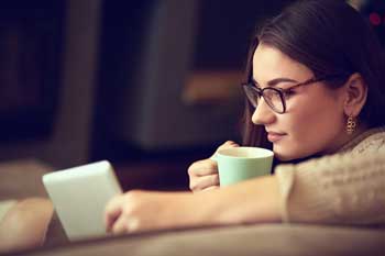 Picture of a lady relaxing with a cup of tea and using a device to shop